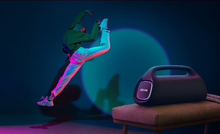 O LG XBOOM GO XG9 está colocado em uma cadeira. Ele projeta uma iluminação cênica na parede, e uma pessoa dança na frente dela.