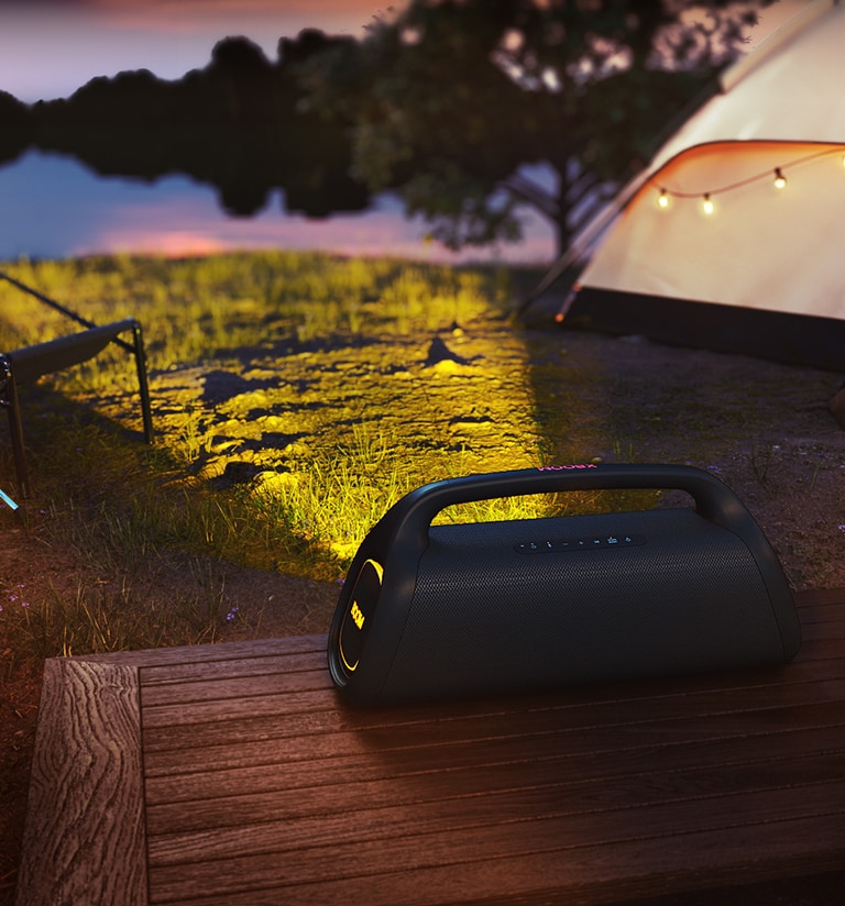 A LG XBOOM GO XG9 está colocada em um deck de madeira. Ela projeta a iluminação cênica no acampamento.