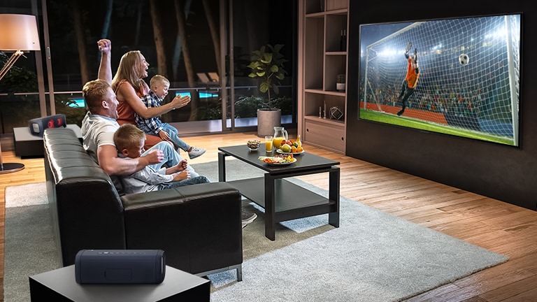 Uma família sentada no sofá assistindo futebol na TV