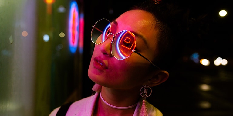 Um close-up de uma mulher usando óculos escuros com luzes de neon refletindo sobre ela.