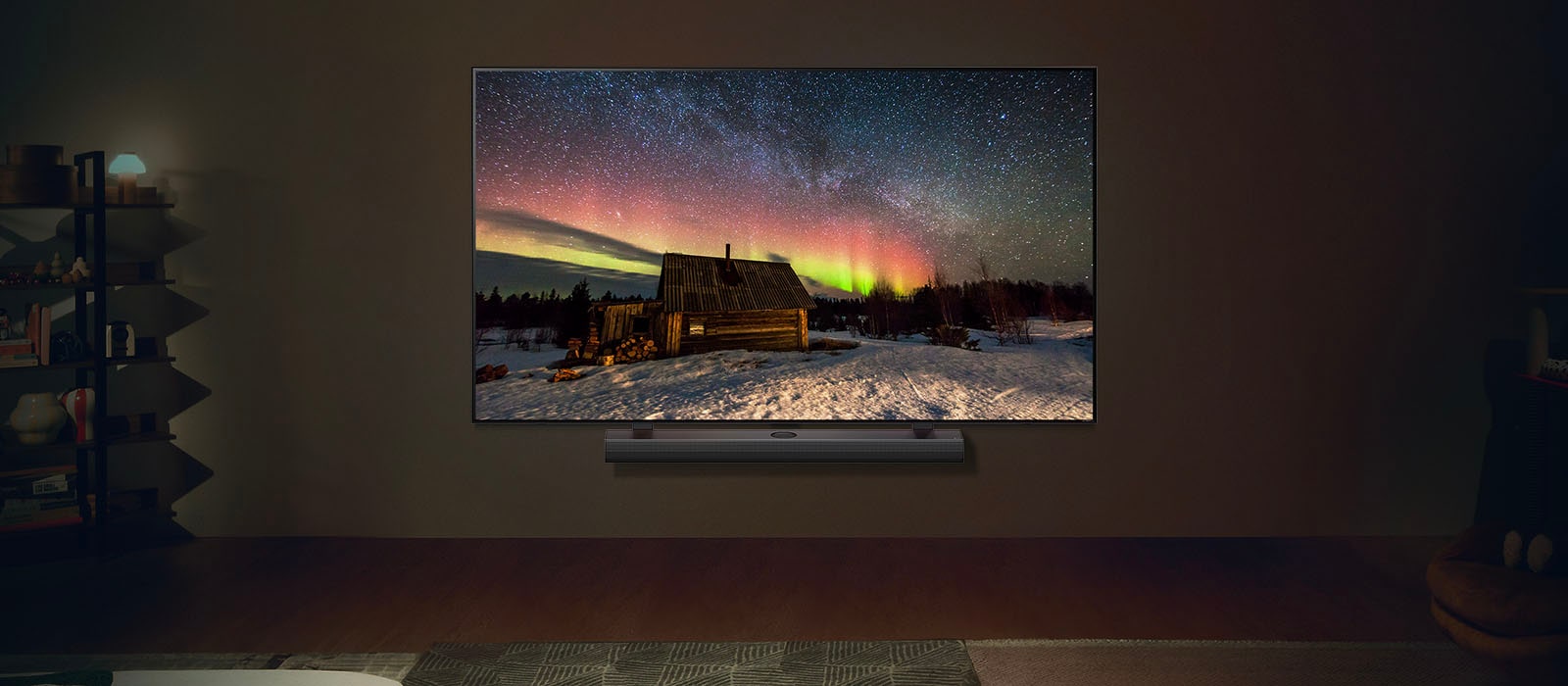 Uma imagem de uma TV e uma Soundbar da LG em um espaço de convivência moderno durante a noite. A imagem de uma aurora boreal é exibida com os níveis ideais de brilho.