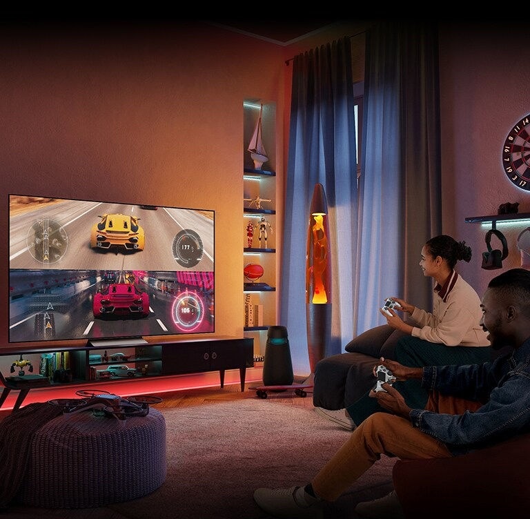 Homem e mulher estão sentados no sofá, curtindo juntos um jogo de corrida automobilística na TV.