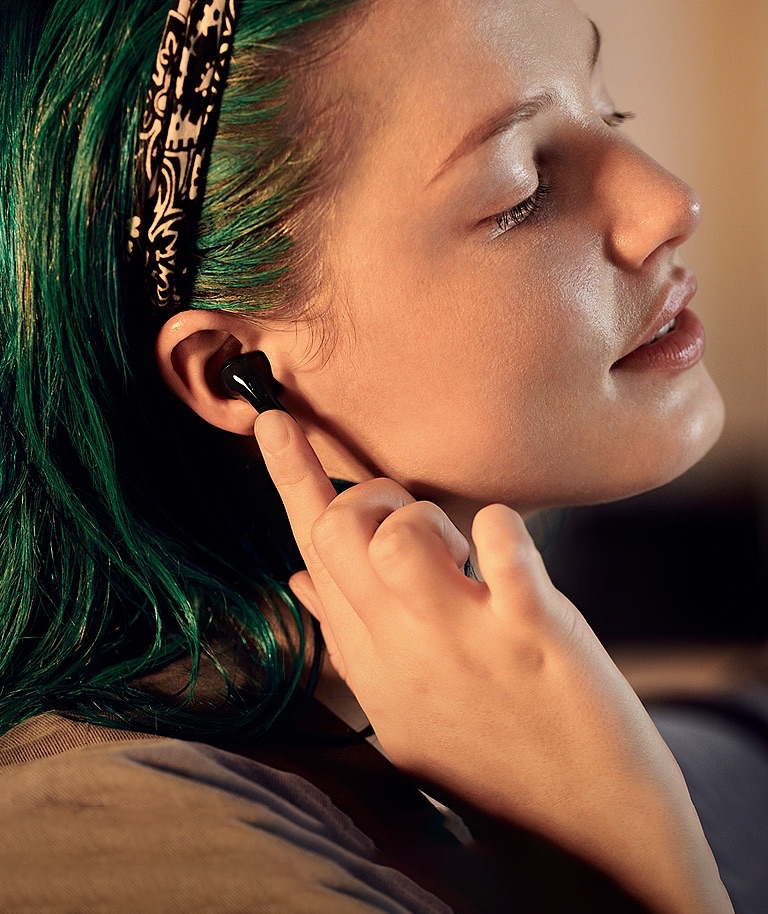 A woman seen in profile. She is wearing T90 earbuds and tapping on one with her finger.