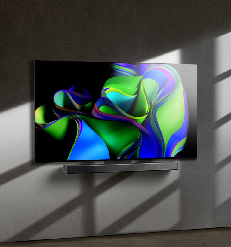 A video opens with the words LG OLED evo against a black background. The words enlargen and fill with colour. Then the scene transitions to LG OLED C3, showing a colourful abstract artwork with a Soundbar against a white background. The white background becomes a wall in a room to which the TV attaches.