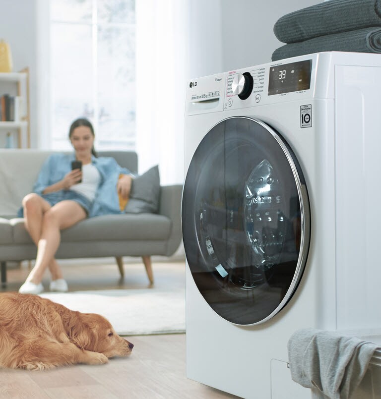 A side view of the washer sits to one side with a dog and a woman on her phone on the other side.