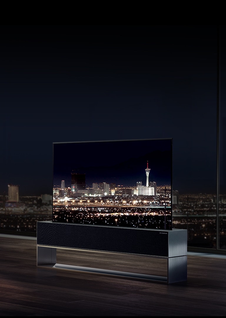 Un homme regarde le téléviseur OLED enroulable de LG SIGNATURE face à la vue nocturne de la ville de Las Vegas dans son salon.