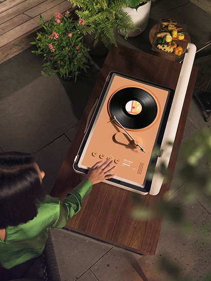 StanbyME Go 被放在木桌上，螢幕上顯示珊瑚主題黑膠唱盤轉音樂造型。