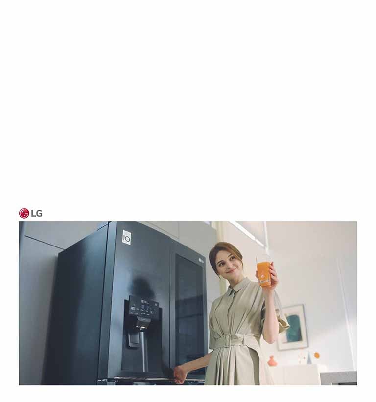 Seorang wanita berdiri di depan kulkas sambil memegang segelas jus dan tersenyum saat menutup pintu.