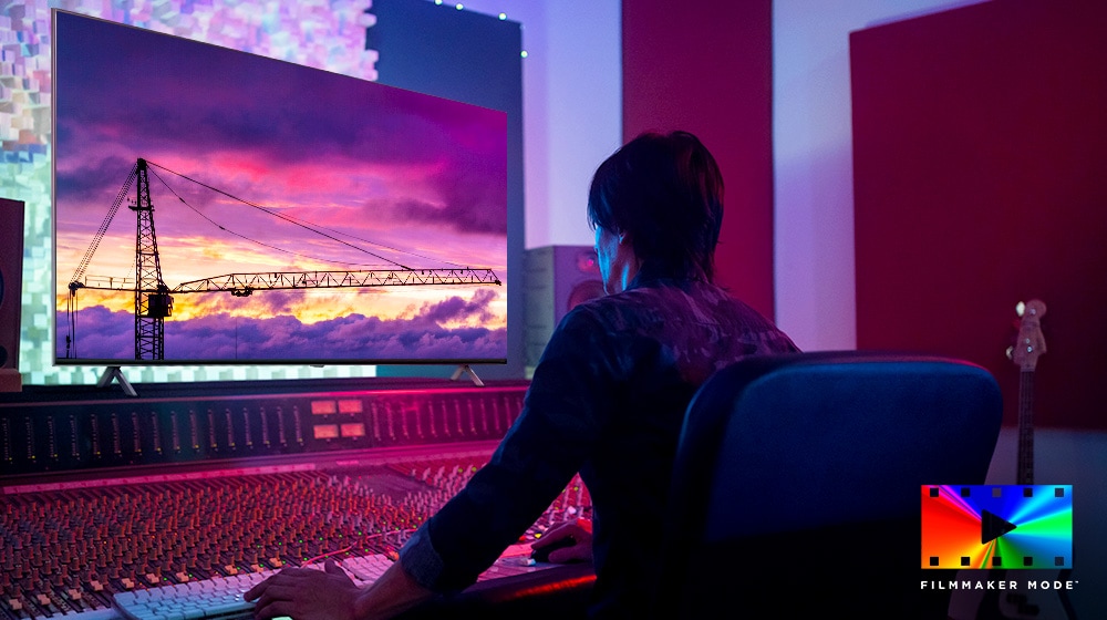 Seorang sutradara film sedang melihat monitor TV besar, mengedit sesuatu. Layar TV menayangkan crane menara di langit berwarna ungu. Logo Mode FILMMAKER ditempatkan di sudut kanan bawah.