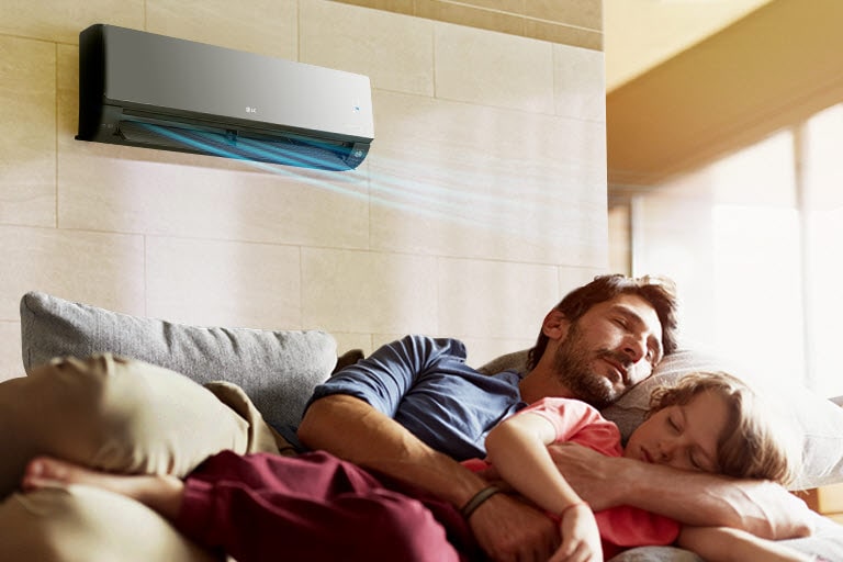 Un padre e una figlia dormono sul divano sotto a un condizionatore che emette aria su di loro.