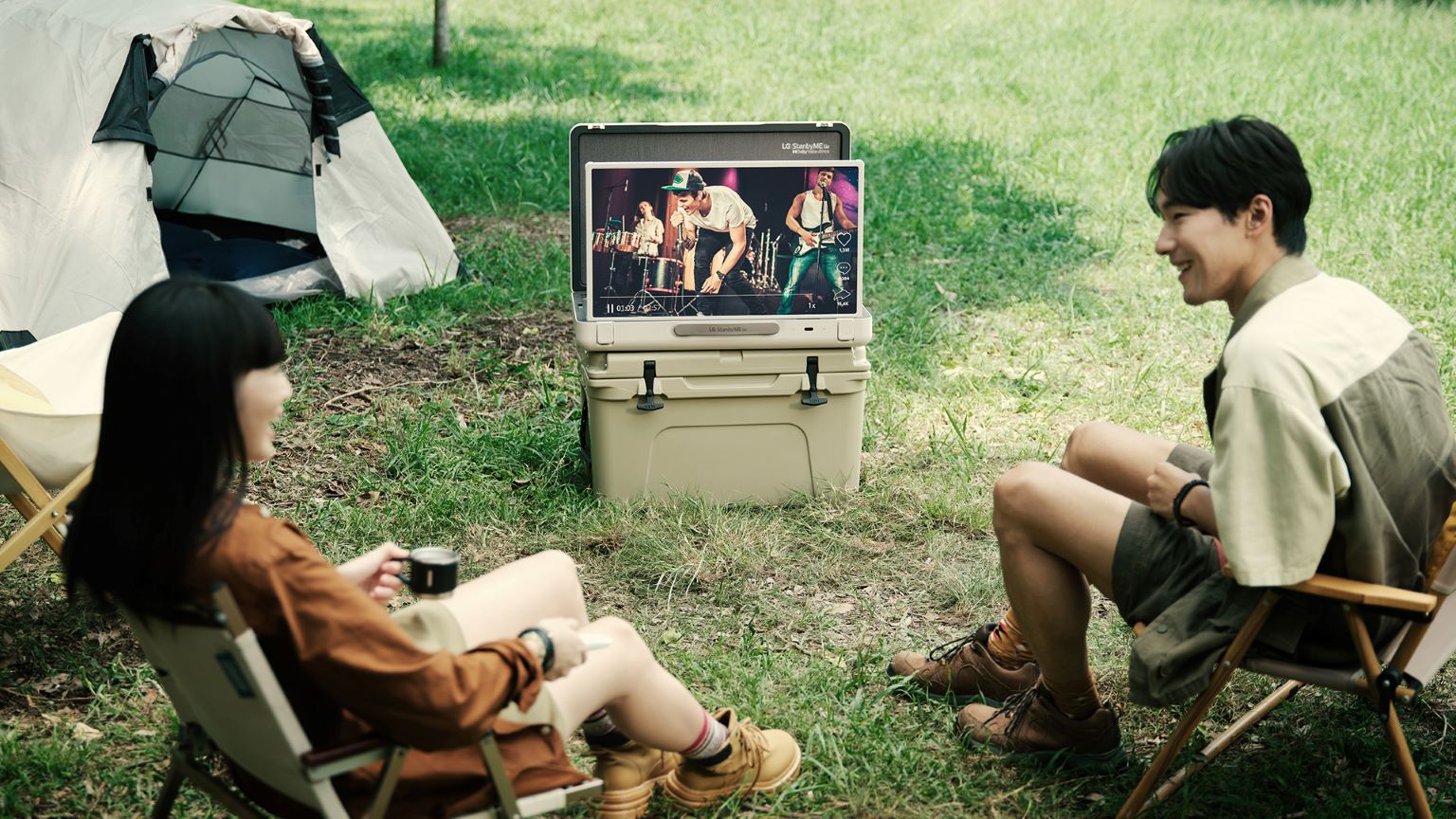 Accessori campeggio: immagine di due ragazzi al campeggio che guardano un video musicale sul tv portatile LG StanbyMe Go