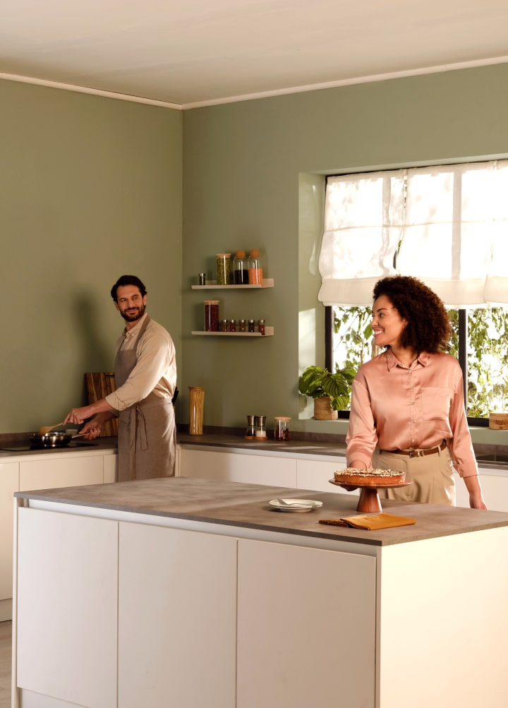 Immagine di una cucina arredata con un uomo ai fornelli e una donna che sta prendendo una torta dal tavolo