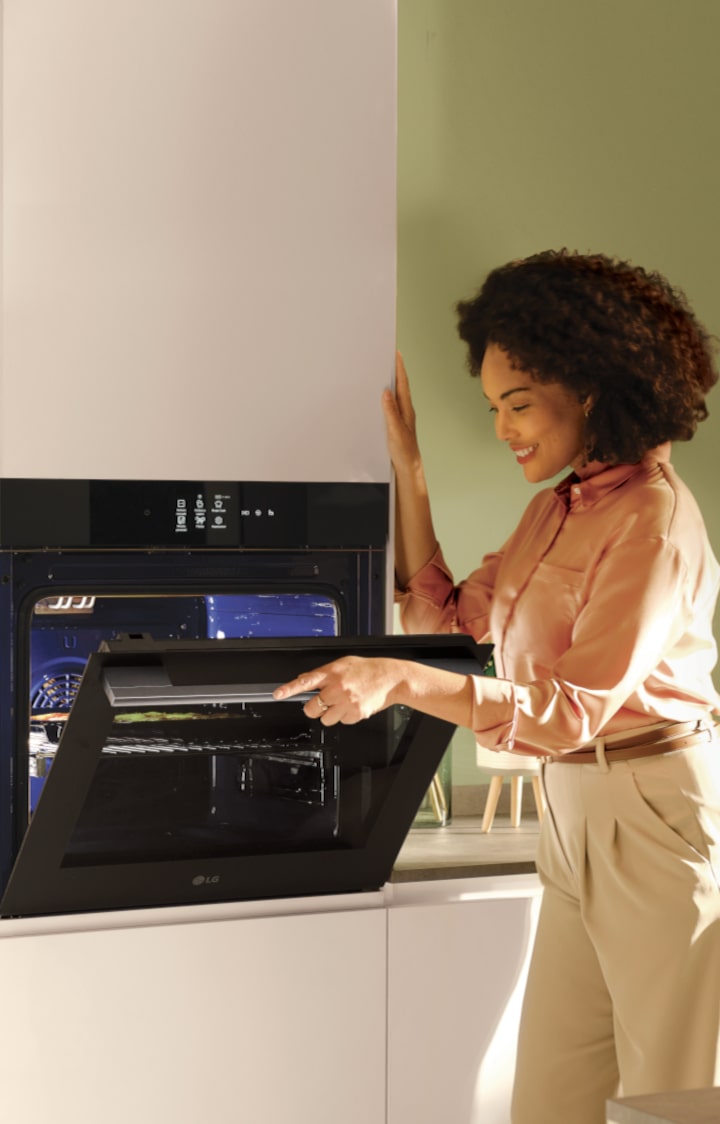 Immagine di una donna che apre il forno e guarda al suo interno con sguardo compiaciuto.