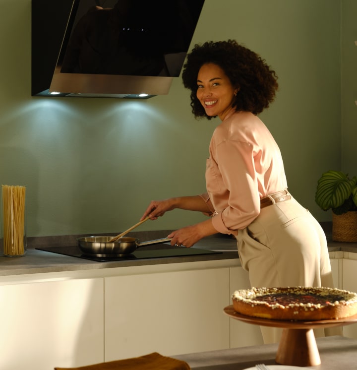 Immagine di una donna che sta cucinando sul piano cottura a induzione, mentre sorride guardando l'obiettivo.
