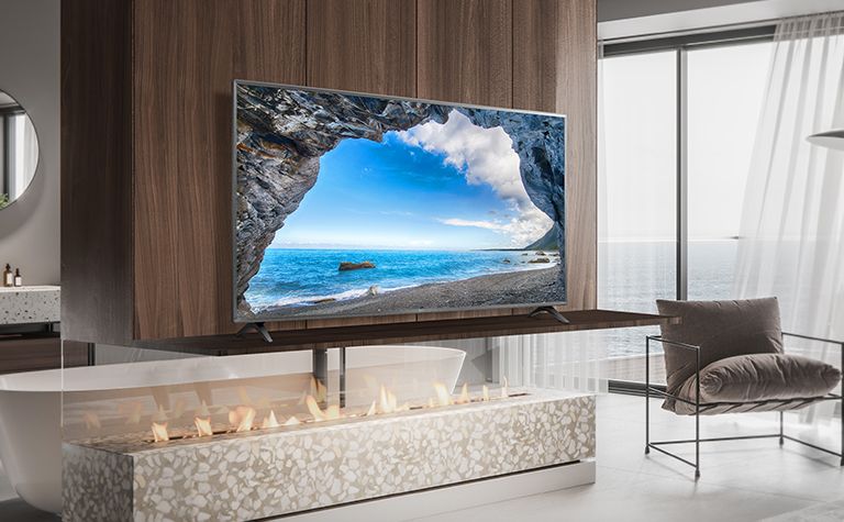 En un dormitorio sencillo con vistas al mar, hay un televisor en un estante de pared. El paisaje azul del mar aparece brillante y claro en la pantalla del televisor.