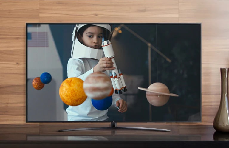 La pantalla de un televisor que reproduce un video de un niño con un traje de astronauta hecho por él, jugando con una nave espacial en su habitación decorada con miniaturas de planetas (reproducir el video)