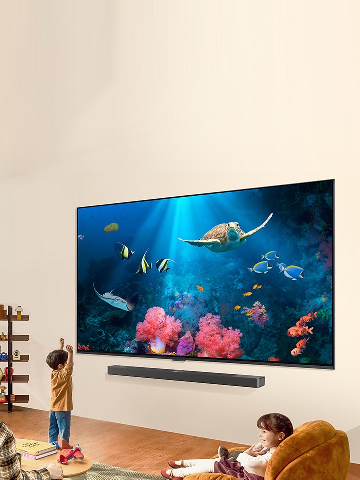A family is watching a bright aquatic scene on a LG QNED TV with a LG Soundbar, in a bright and natural living space.