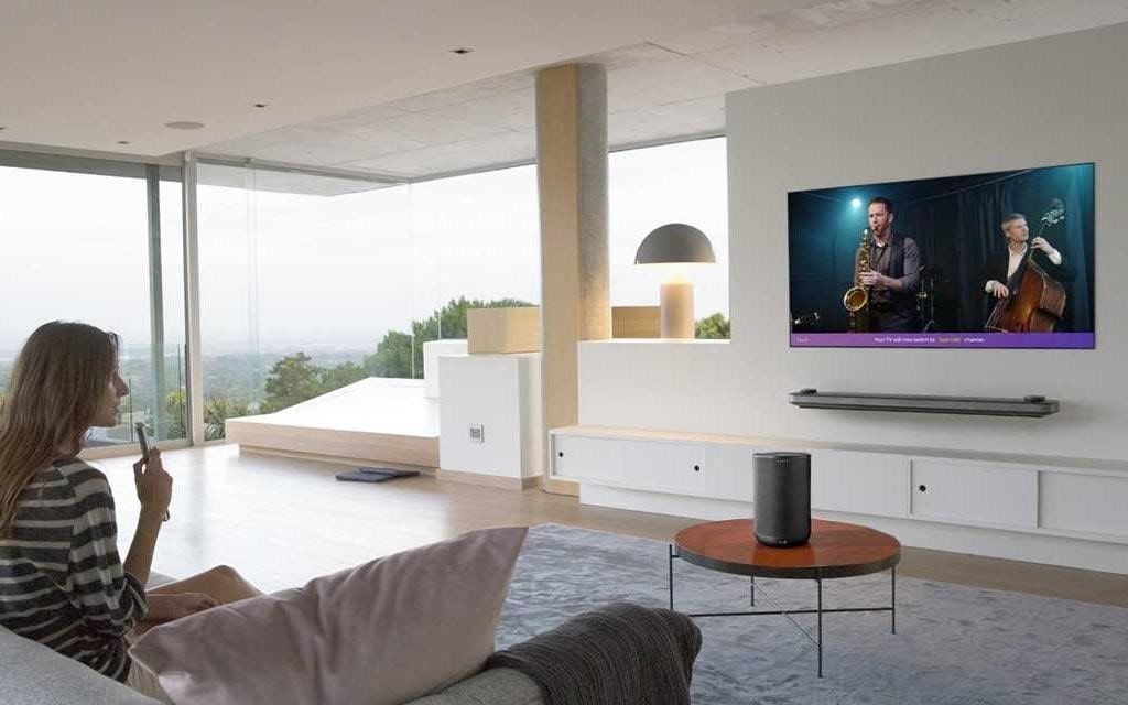 Eine Frau sitzt in ihrem Wohnzimmer und nutzt die LG-Fernbedienung, um mit ihrem LG OLED Wallpaper TV zu sprechen.