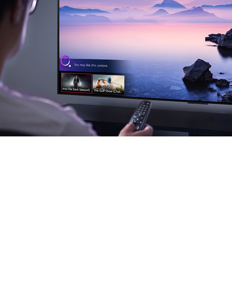 Gros plan d’un homme en train de choisir ce qu’il va regarder sur un téléviseur avec une télécommande, tandis qu’un paysage est affiché sur le téléviseur