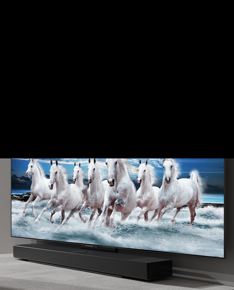 La barra de sonido y el televisor están sobre la mesa blanca y se muestran 7 caballos blancos en el televisor.