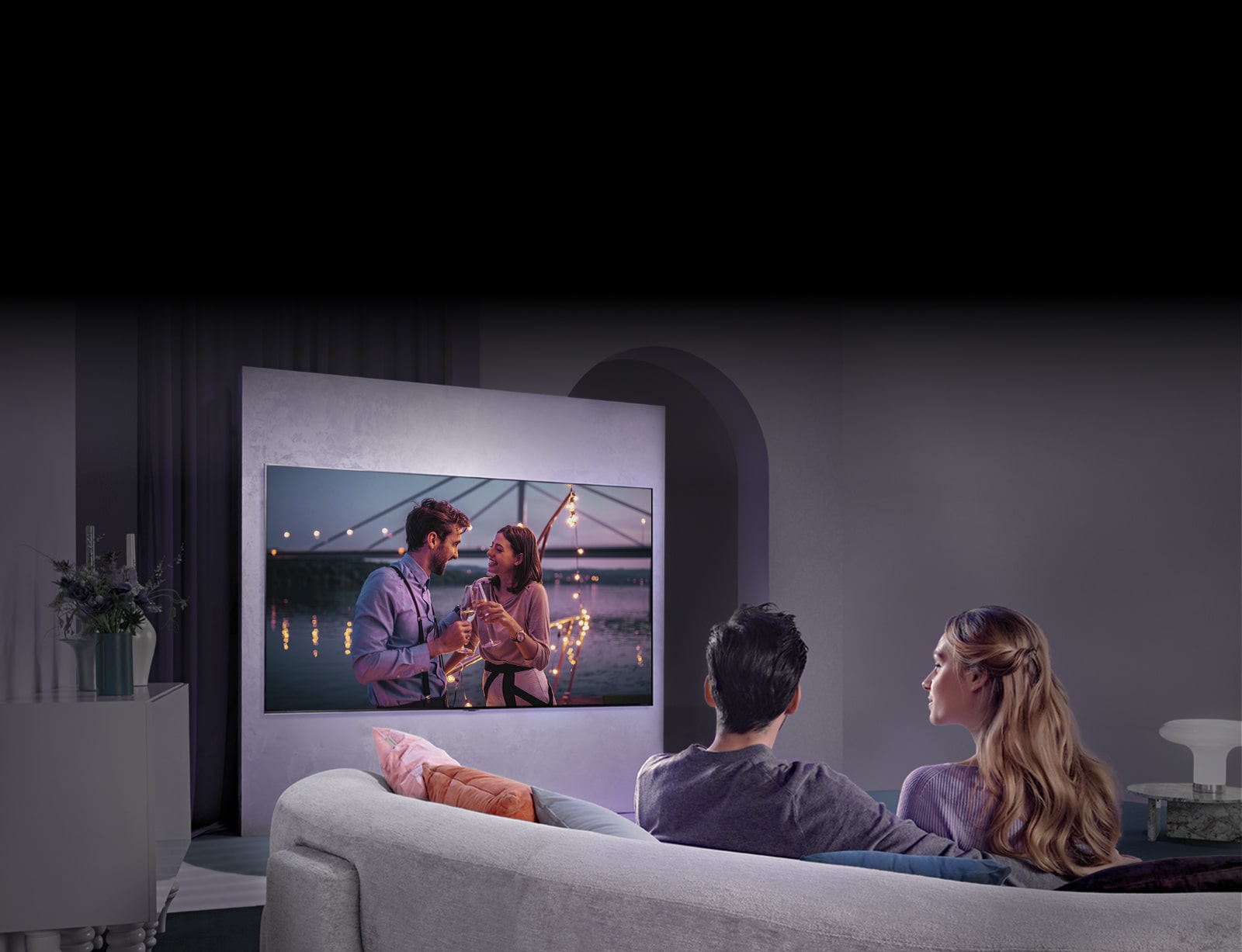 Una persona sentada en un sofá está disfrutando de una película en un gran televisor colgado en la pared.