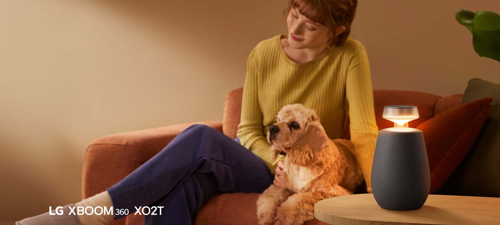 Una mujer sentada en el sofá con su perro y escuchando música con LG XBOOM 360 XO2T.