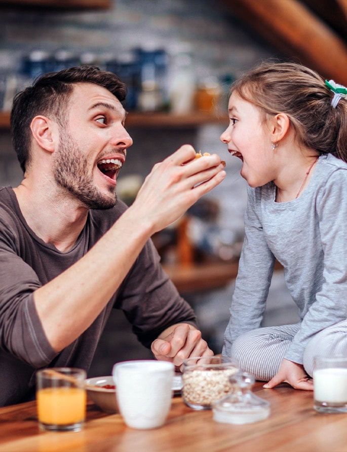 An image of a father feeding his daughter snack joyfully.