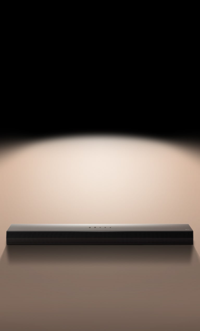 LG Soundbar μπροστά από μαύρο φόντο που φωτίζεται με προβολέα. 
