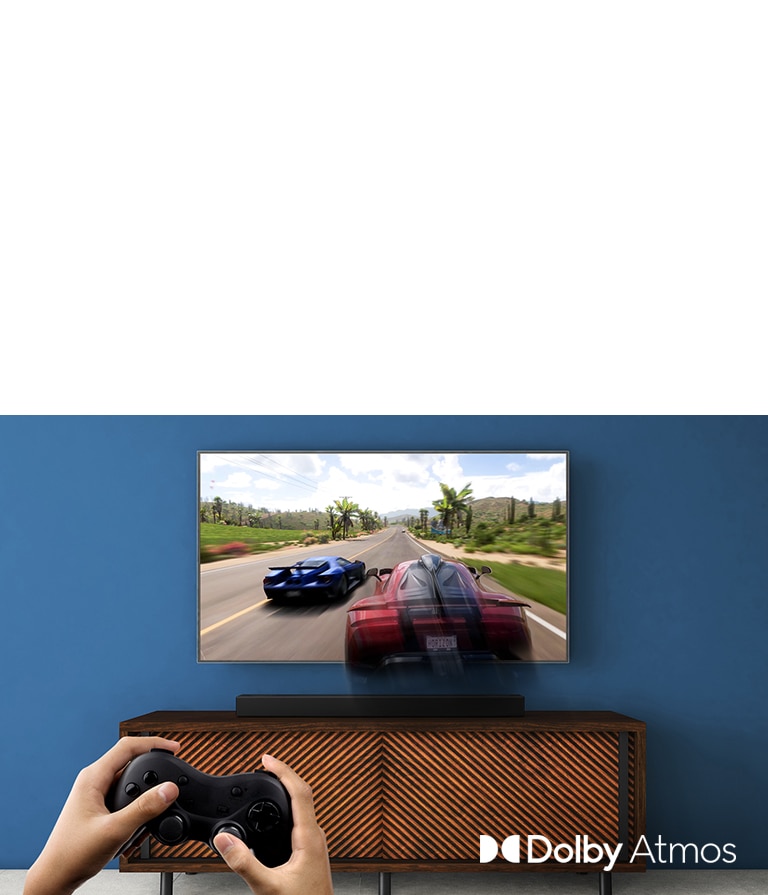 LG TV-en henger på veggen og viser et racerspill. LG Sound Bar er plassert på den brune hylla rett nedenfor LG TV-en. En mann holder en spillkontroll. NYTT merke vises oppe i venstre hjørne.