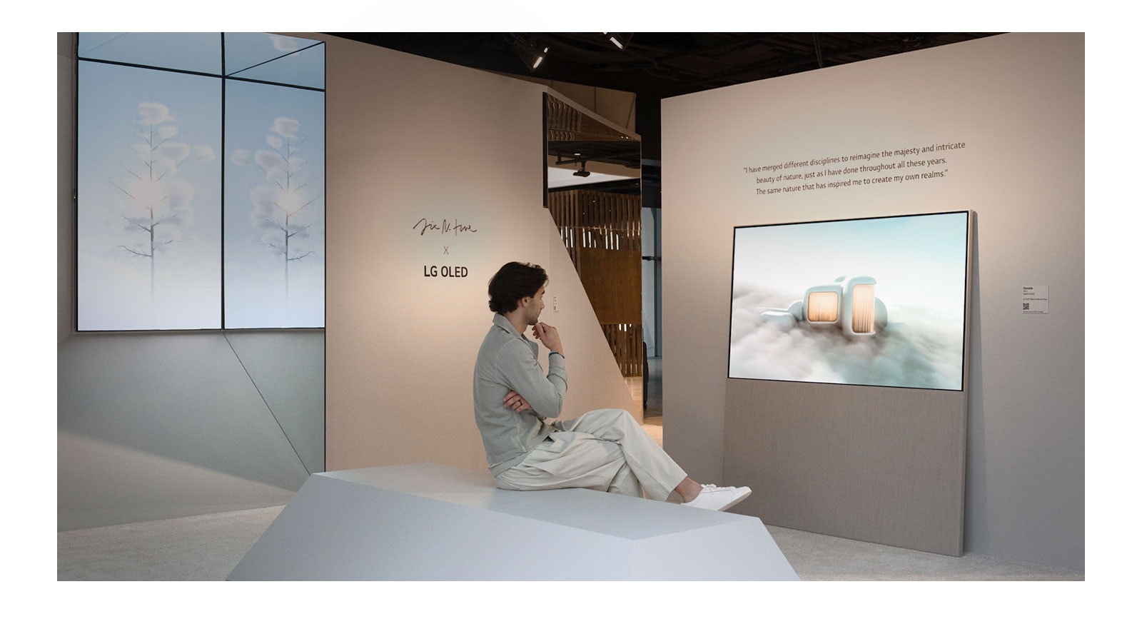 The image shows a person sitting on a chair looking at dreamlike scenery set among the clouds playing on Easel. On another wall, an LG OLED display shows an image of snow-covered trees reaching into the sky.