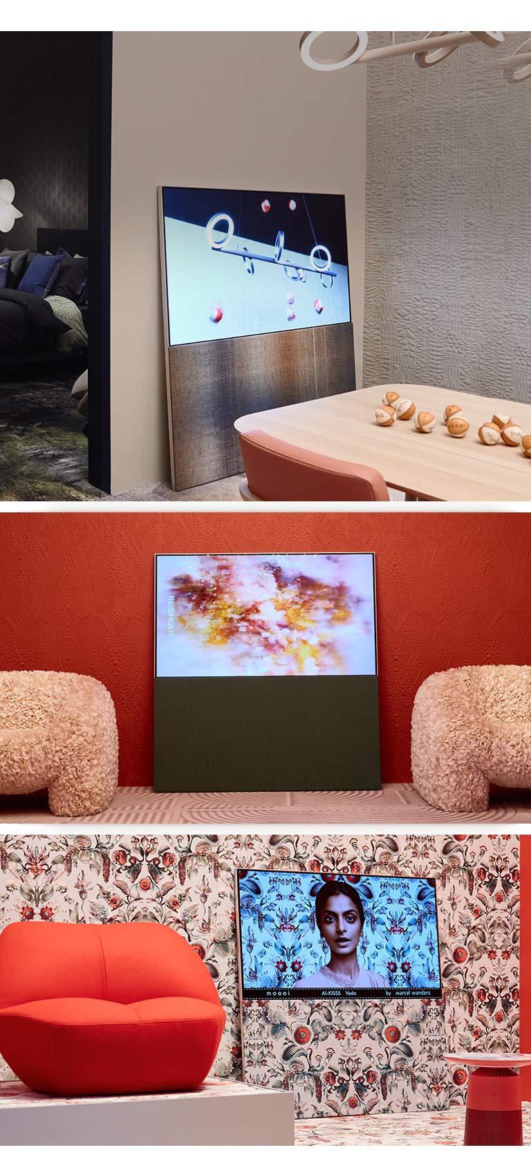 The top image shows Easel leaning against a wall in a neutral-colored room showing an abstract artwork featuring baseballs on the screen. Across from the TV sits a wooden table that also has baseballs on it. 	 The bottom right image shows Easel leaning against a bright floral patterned wall with a red and green color scheme. A picture of a woman against the same background as the surrounding wall is on the screen. The fabric textured stand also has the same pattern. Beside the TV, there is a red one-person sofa. The bottom left image shows Easel leaning against a textured terracotta-colored wall. An abstract red, orange, and purple image fills the screen. On either side of the TV, there are beige, textured one-person sofas.