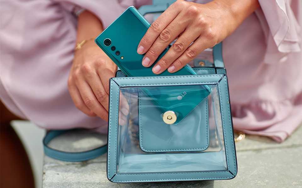 A woman is putting an LG VELVET smartphone in her bag.