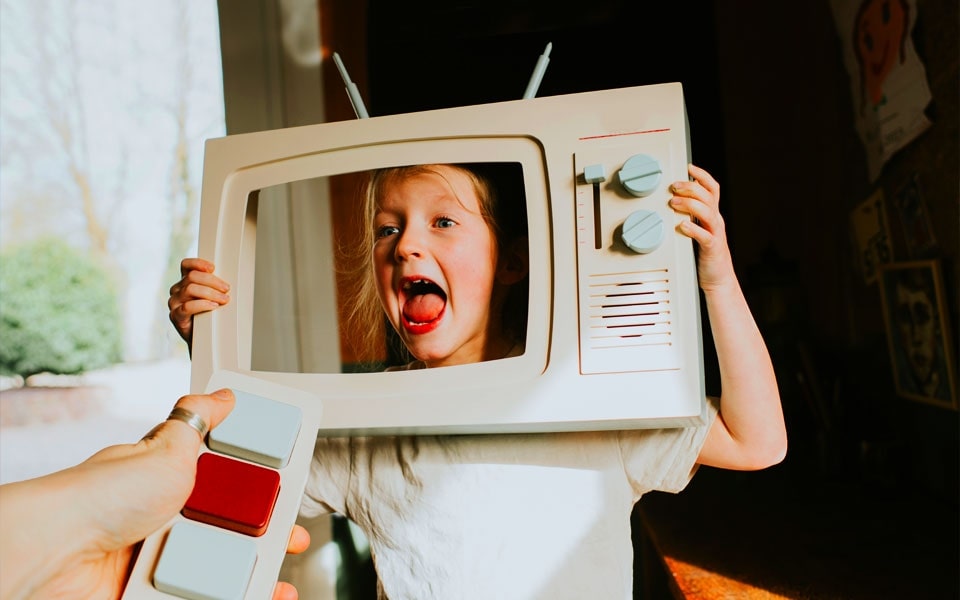 Criança segurando um televisor recortado com um adulto segurando um comando de televisão de brinquedo, representando o processo de calibração de um televisor