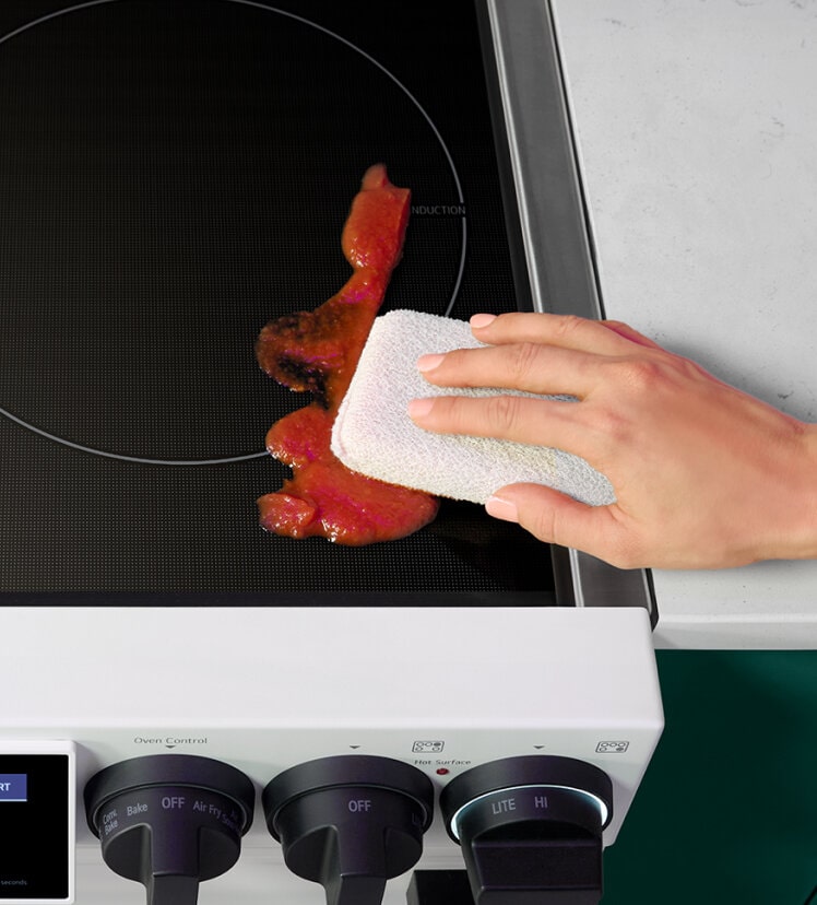A person using a cloth to easily wipe down an LG induction cooktop.